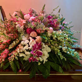 Large pink and white flower casket spray with orchids and lilies on a closed wooden casket