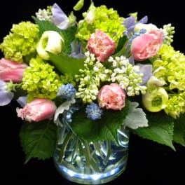 Low glass vase of pink fringe tulips, green hydrangeas, lilac, and pastel blooms in a rounded arrangement