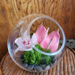 Pink orchid and calla lilies in a clear glass orb with stones
