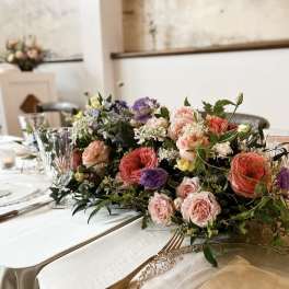 Low floral centerpiece with pink, peach, purple, and white blooms on a table