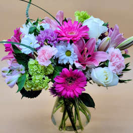 Mixed pink, white, and green flowers arranged in a clear glass vase