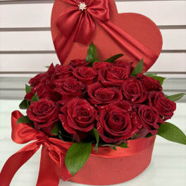 Red roses arranged in a heart-shaped box with a satin bow