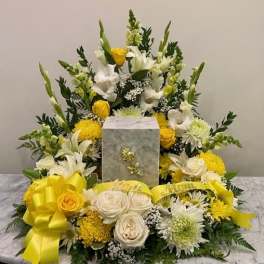 Yellow and white floral funeral arrangement with a gray urn centerpiece
