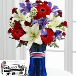 Bouquet of red gerbera daisies, white lilies, and purple irises in a blue vase