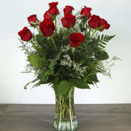 Red roses arranged in a clear glass vase with greenery
