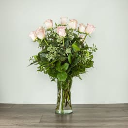 Pink roses in a clear glass vase with mixed greenery