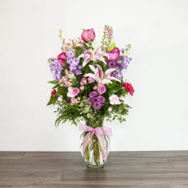 Tall bouquet of pink and purple flowers in a glass vase with a pink ribbon