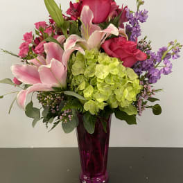 Pink lilies, roses, hydrangea, and purple flowers in a magenta vase