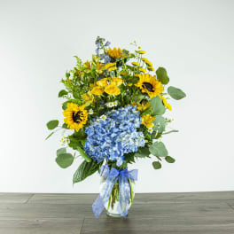 Bouquet of sunflowers, blue hydrangea, and yellow blooms in a glass vase