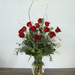 Red roses arranged in a clear glass vase with greenery