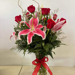 Red roses and pink lilies in a glass vase with a red ribbon