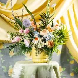 Colorful mixed flower arrangement in a yellow vase on a draped table