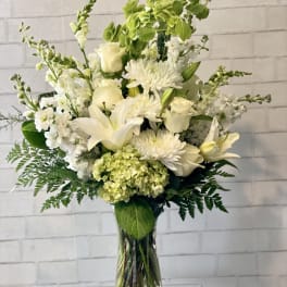 White floral arrangement in a clear glass vase with lilies, roses, and chrysanthemums