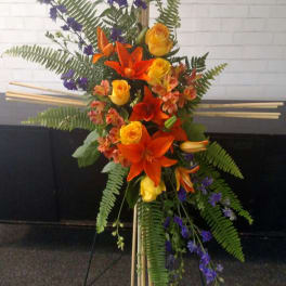 Tall floral standing arrangement with orange lilies, yellow roses, and purple flowers
