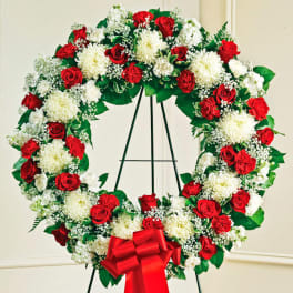 Red and white floral wreath on a black stand with a red bow