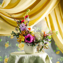 Asymmetrical mixed flower arrangement with pink, yellow, and white blooms in a small white vase.