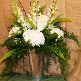White floral arrangement in a tall glass vase with fern accents