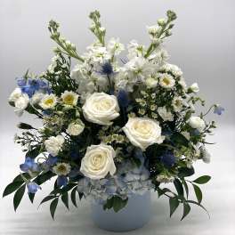 White and blue arrangement with roses, hydrangeas, and daisies in a light blue cylinder vase