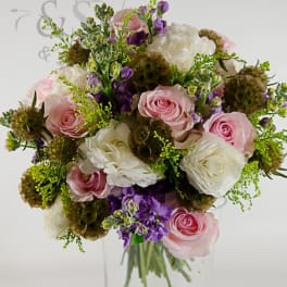 Pink and white roses with purple flowers in a clear glass vase