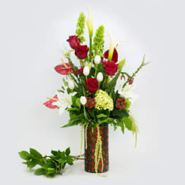 Tall floral arrangement with red roses, white lilies, and green accents in a patterned vase