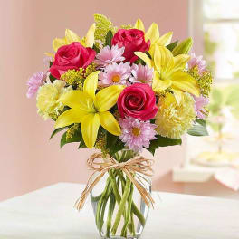 Bouquet of pink roses, yellow lilies, and daisies in a clear glass vase