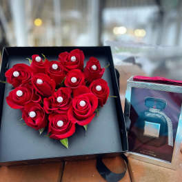 Heart-shaped box of red roses beside a perfume gift box