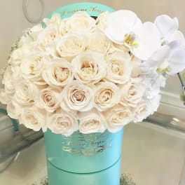 White roses and orchids arranged in a turquoise hat box