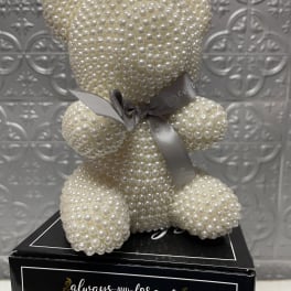 Pearl-covered teddy bear with a ribbon on a black box