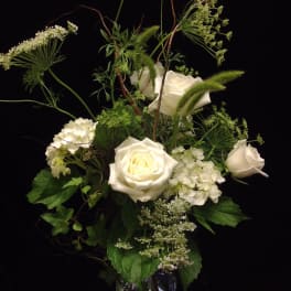 Tall arrangement of white roses and hydrangeas with airy filler in a clear glass vase