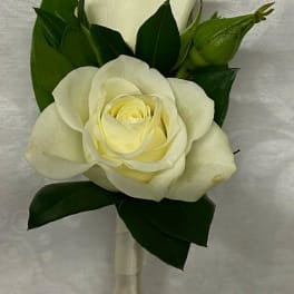 White rose boutonniere with dark green leaves and satin ribbon