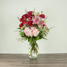 Bouquet of red roses, pink lilies, and pale hydrangea in a clear glass vase