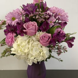 Pink and purple bouquet with roses, hydrangea, and daisies in a purple vase