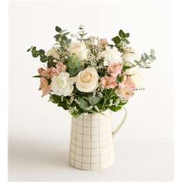 Bouquet of cream and blush flowers in a checkered pitcher vase