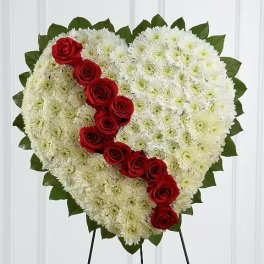 Heart-shaped white floral spray with red roses on a stand