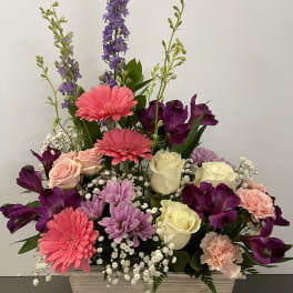 Mixed bouquet in a white rectangular container with pink, purple, and cream flowers