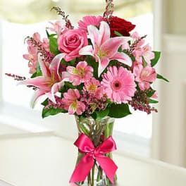 Pink and red mixed flowers in a clear glass vase with a ribbon