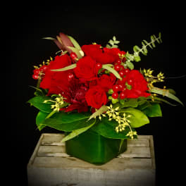 Red rose arrangement in a green vase with berries and greenery