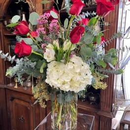 Tall bouquet of red roses, white hydrangea, and eucalyptus in a glass vase
