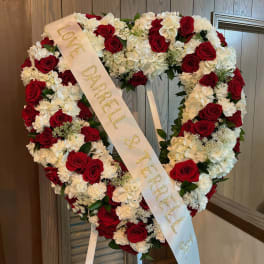 Heart-shaped wreath of red roses and white flowers with a memorial ribbon