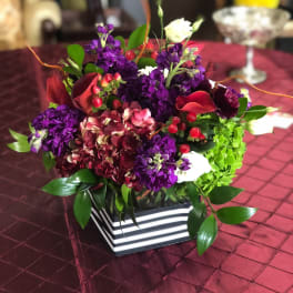 Mixed purple and red floral arrangement in a striped square box