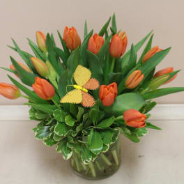 Orange tulips arranged in a glass vase with a small butterfly decoration