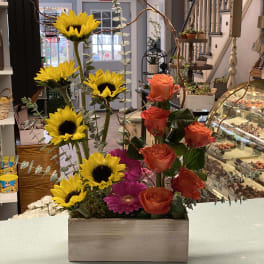 Mixed bouquet with sunflowers, orange roses, and pink gerbera daisies in a wooden box