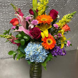 Colorful mixed bouquet in a glass vase with roses, lilies, gerbera daisies, and hydrangea