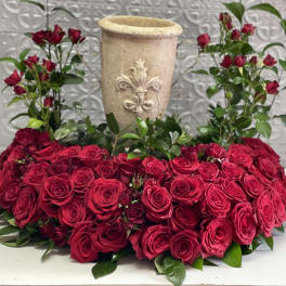 Heart-shaped red rose arrangement with a tall beige vase in the center