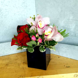 Red roses and pale pink orchids in a black square vase