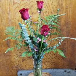 Three red roses in a clear glass vase with airy greenery
