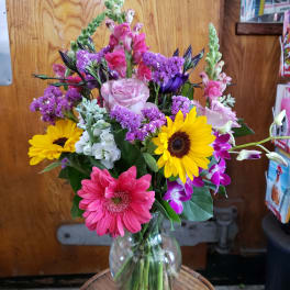 Mixed bouquet in a clear glass vase with pink, yellow, purple, and white flowers