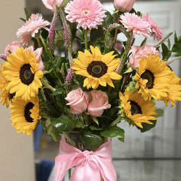 Bouquet of pink roses and yellow sunflowers in a clear vase with a pink ribbon
