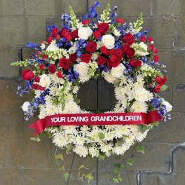 Large funeral wreath of red, white, and blue flowers on an easel
