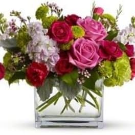 Pink and red roses in a clear square vase with green accents